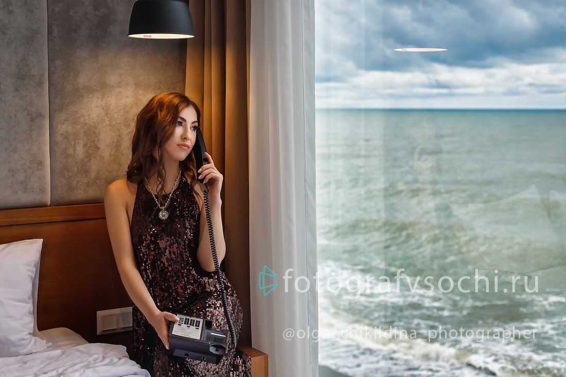 Девушка с телефоном у окна смотрит на море