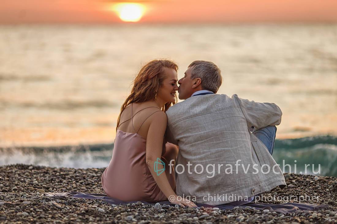 Мужчина и женщина сидят на берегу моря на закате