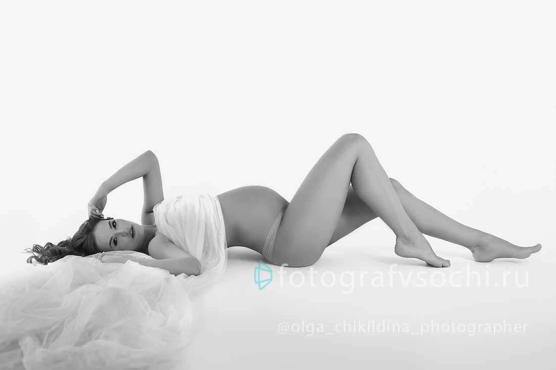 Беременная женщина позирует лежа на полу, фотография монохромная