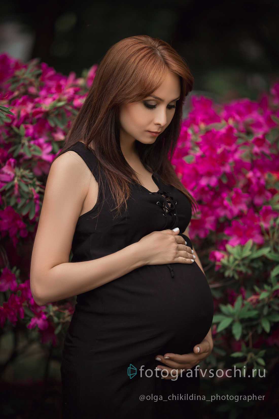 Беременная девушка в черном на фоне ярких цветов