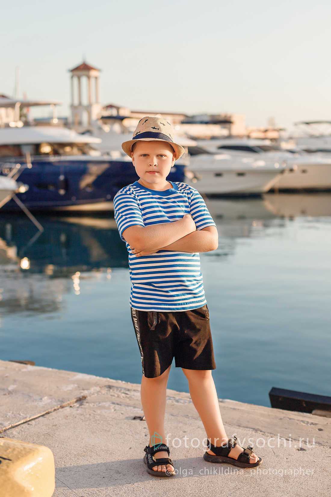 Мальчик в шляпе и полосатой футболке у моря на фоне яхт