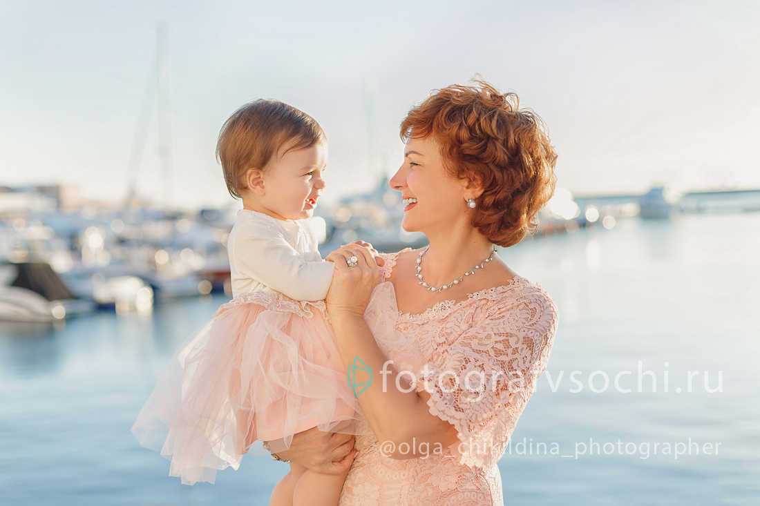 Маленькая девочка на руках у женщины на фоне моря и яхт