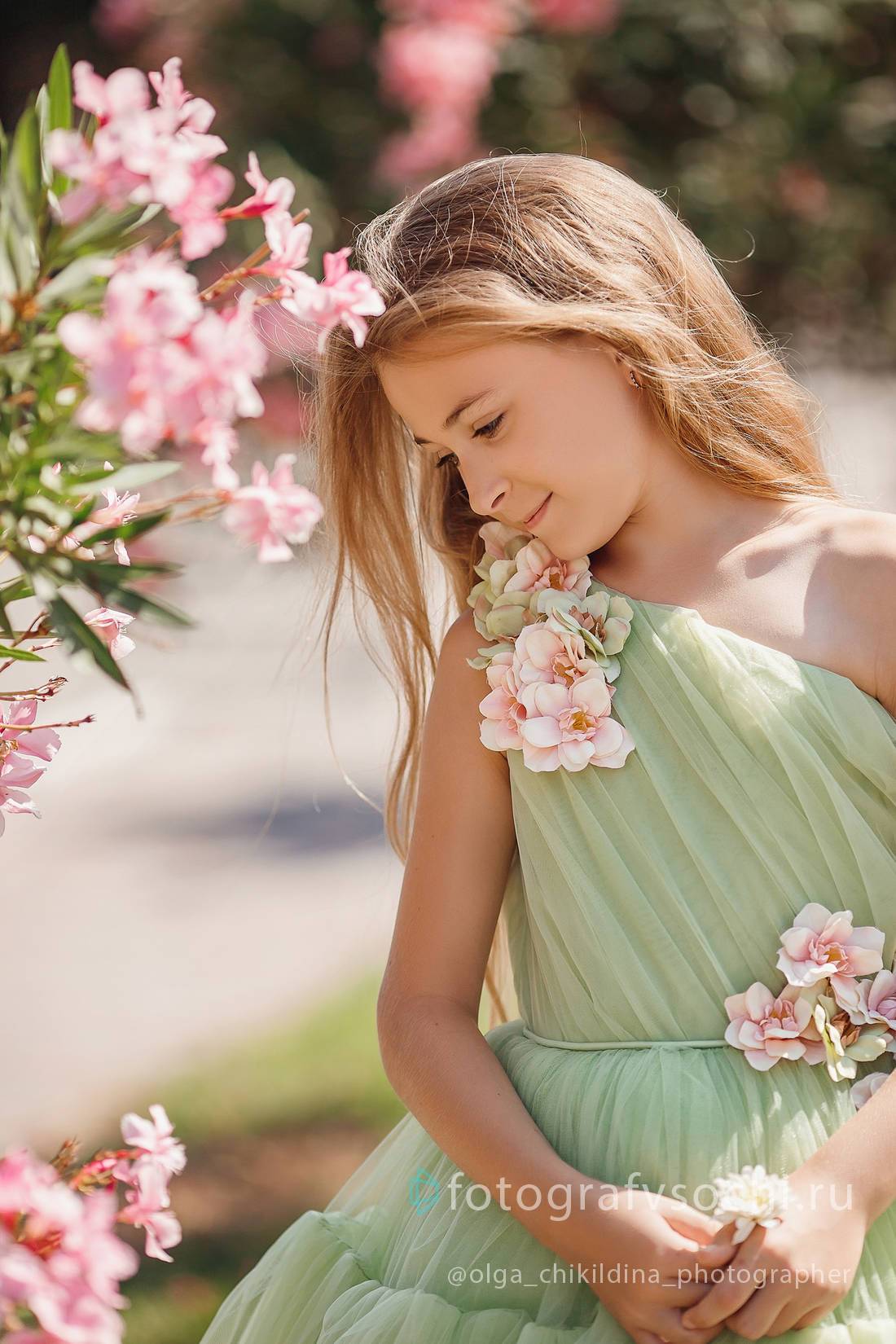 Девочка в зеленом платье у куста с розовыми цветами