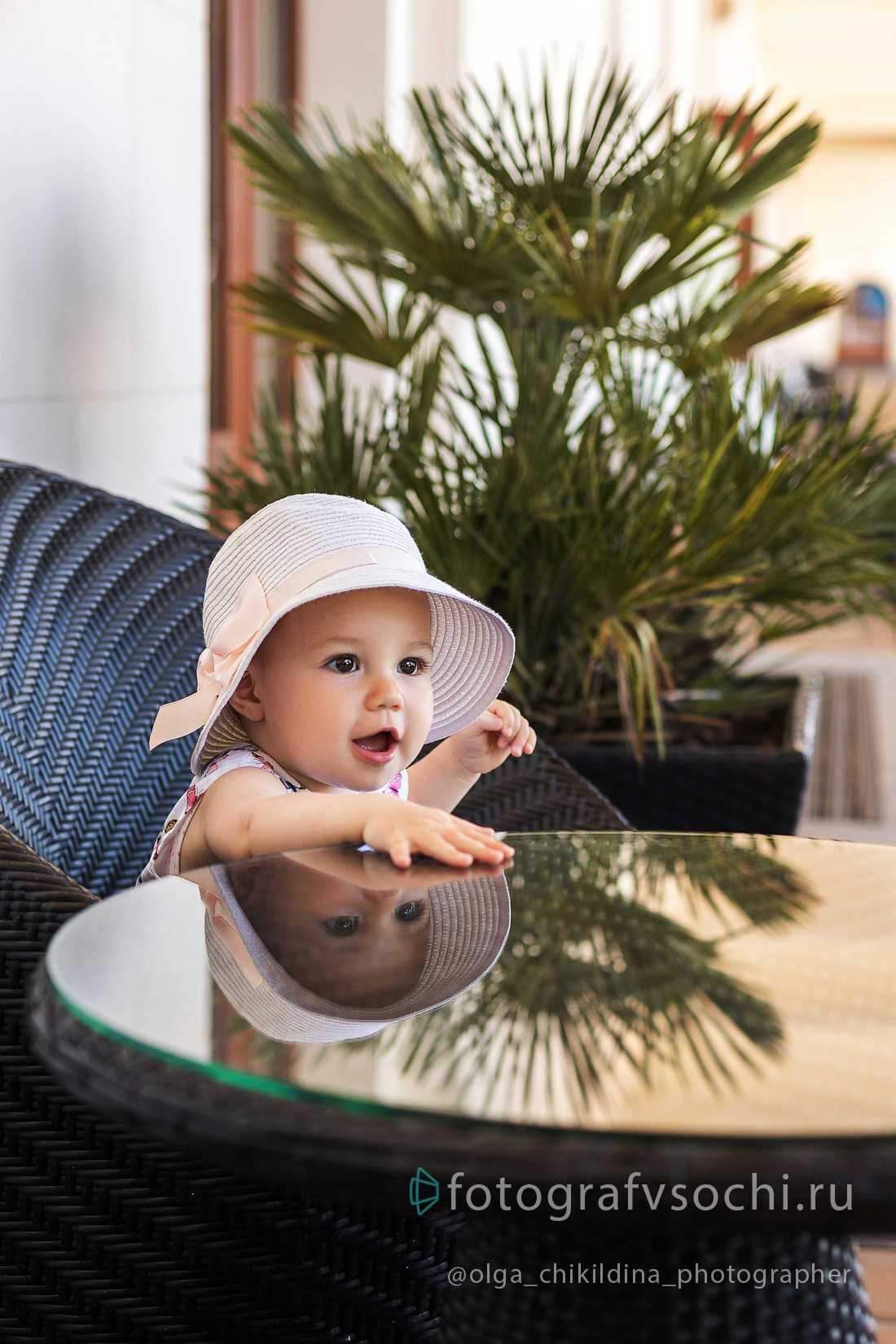 Маленькая девочка в шляпке сидит за стеклянным столом